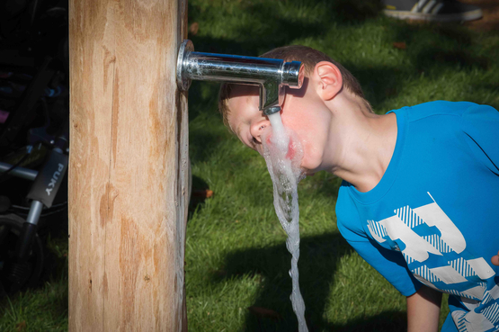 Junge trinkt Wasser aus einem Zapfhan.