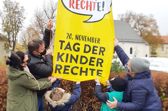 Ausschussvorsitzende GR*in Karin Blum, Bgm. Andreas Babler und die Vorsitzende der Traiskirchner Kinderfreunde GR*in Sabrina Divoky hissen gemeinsam mit zwei Kindern die Fahne für Kinderrechte.