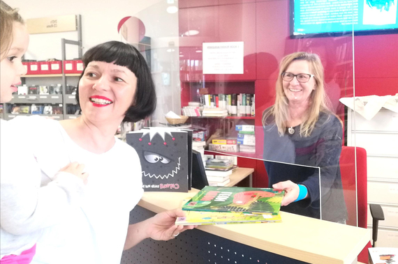 GR*in Karin Blum mit Tochter Flora auf dem Arm und Stadtbibliotheks-Leiterin Christa Majnek bei der Buchausleihe.