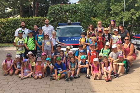 Kindergruppe vor Polizeiwagen.